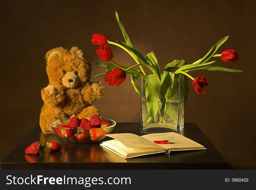 Still-life with tulips, the book and a strawberry on a dark background. Still-life with tulips, the book and a strawberry on a dark background