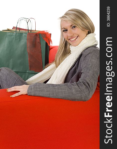 Young, happy woman sitting on couch with shopping bags. Looking at camera, side view. White background.