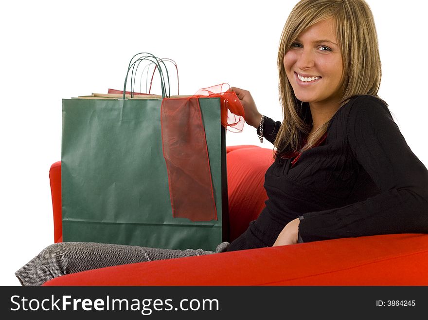 Young, happy woman sitting on couch with shopping bags. Looking at camera, side view. White background. Young, happy woman sitting on couch with shopping bags. Looking at camera, side view. White background.