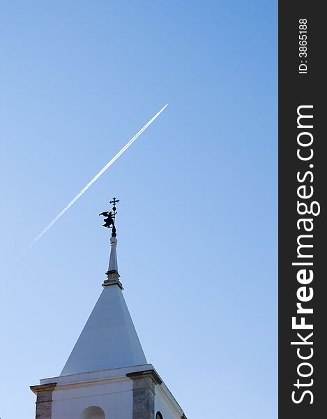 Belfry tower with an angel weather vane pointing to the sky cruise by a jet plane. Belfry tower with an angel weather vane pointing to the sky cruise by a jet plane