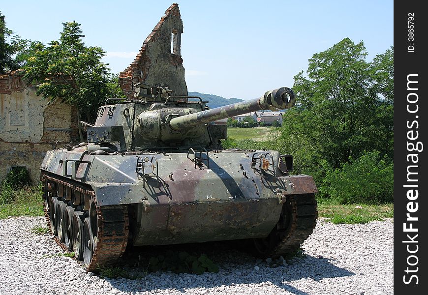 A army tank in front of a ruin.