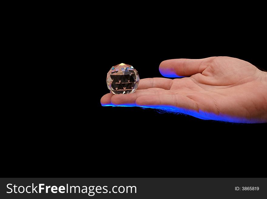 Multi faceted crystal globe sitting on finger tips of a man lit from below with blue theatrical lighting against a black background. Multi faceted crystal globe sitting on finger tips of a man lit from below with blue theatrical lighting against a black background