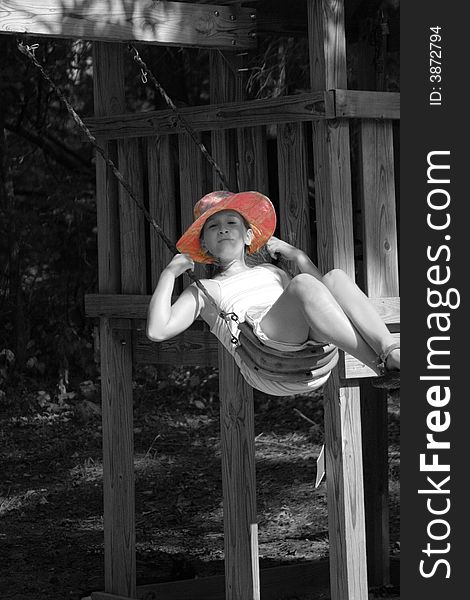 A young girl swings on a swingset with a pink summer hat and selective saturation