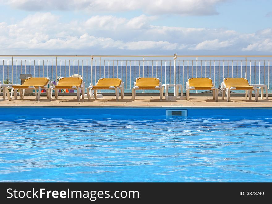 Pool sunbeds around a pool with sea in background