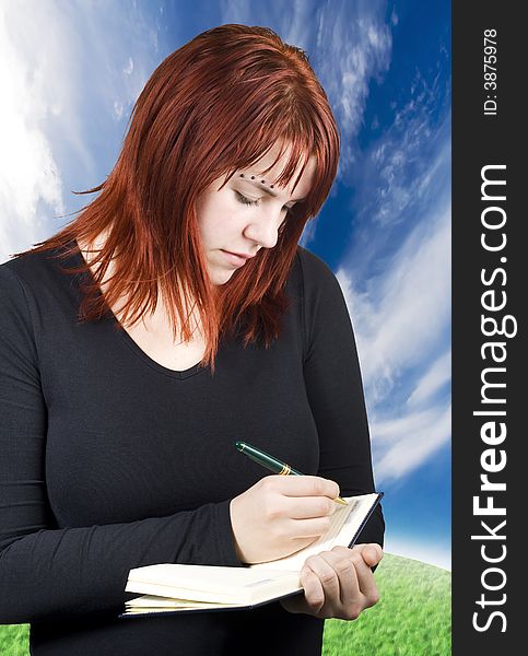 Cute redhead writing in her notebook or diary