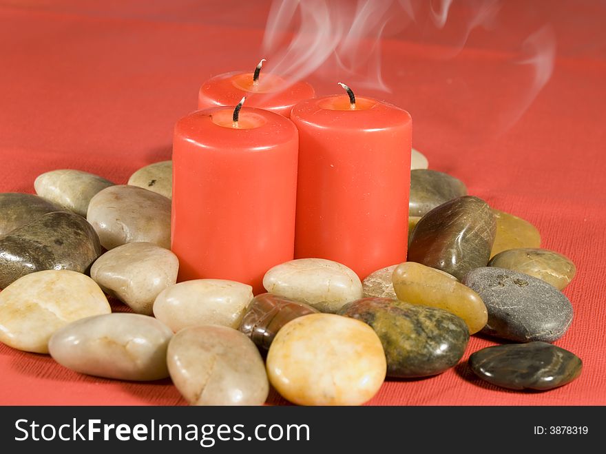 Three red candles smoking in a pile of river rocks isolated against a red background. Three red candles smoking in a pile of river rocks isolated against a red background