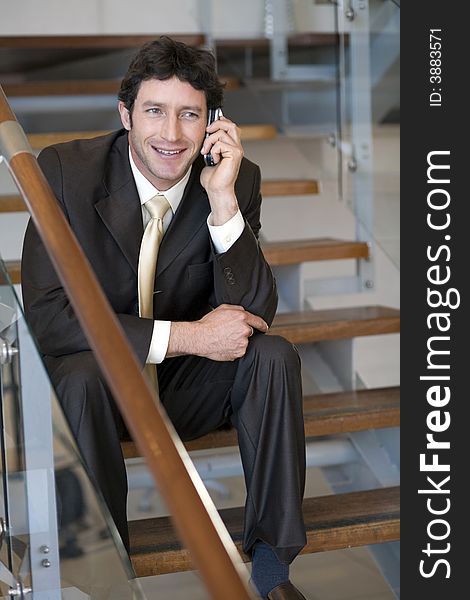 Mature businessman talking on cellphone whilst sitting on stairs