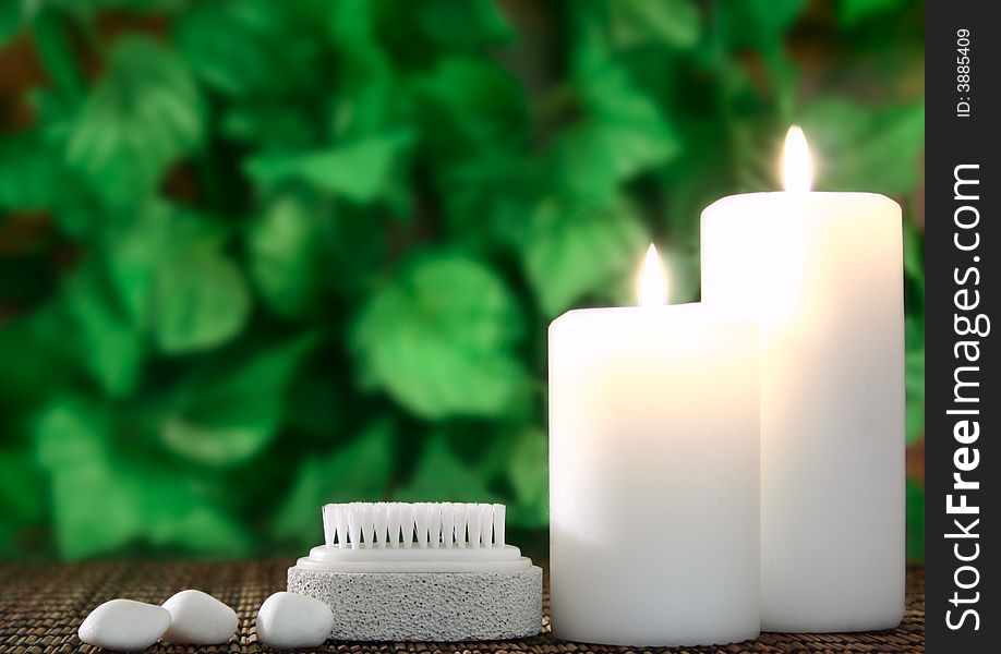 Two white candles,a pumice and a few white stones before green leaf. Two white candles,a pumice and a few white stones before green leaf