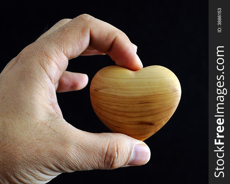 Man's hand holding a heart against black background