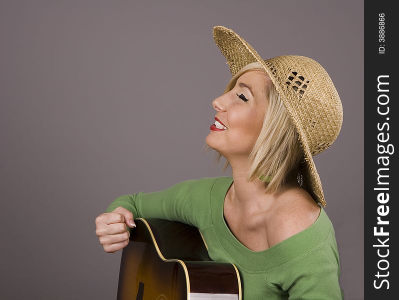 A blonde with a straw hat and guitar pumping her fist in triiumph. A blonde with a straw hat and guitar pumping her fist in triiumph