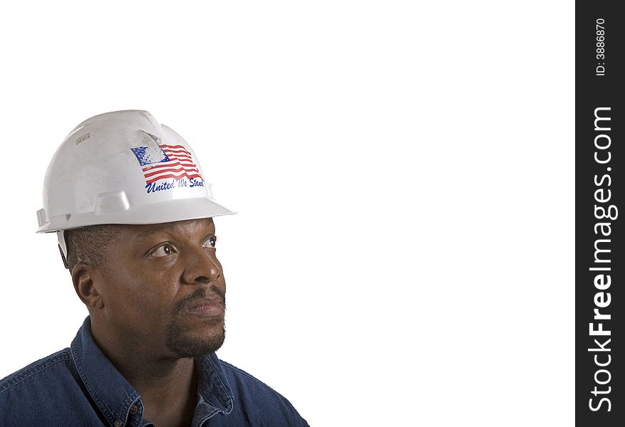 A black construction worker in blue denim shirt and white hard hat looking up into copy space. A black construction worker in blue denim shirt and white hard hat looking up into copy space