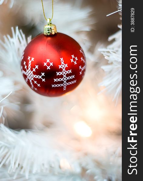 Red bauble with snowflakes and Christmas tree designs hanging on a white Christmas tree