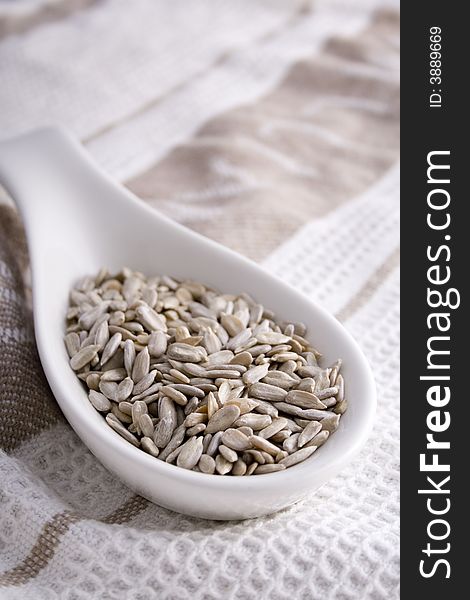 Pumpkin seeds (pepitas) in a white serving spoon on a beige and white cloth. Pumpkin seeds (pepitas) in a white serving spoon on a beige and white cloth