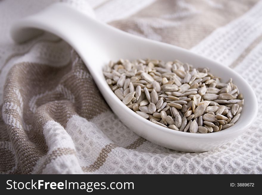 Pumpkin seeds (pepitas) in a white serving spoon on a beige and white cloth. Pumpkin seeds (pepitas) in a white serving spoon on a beige and white cloth