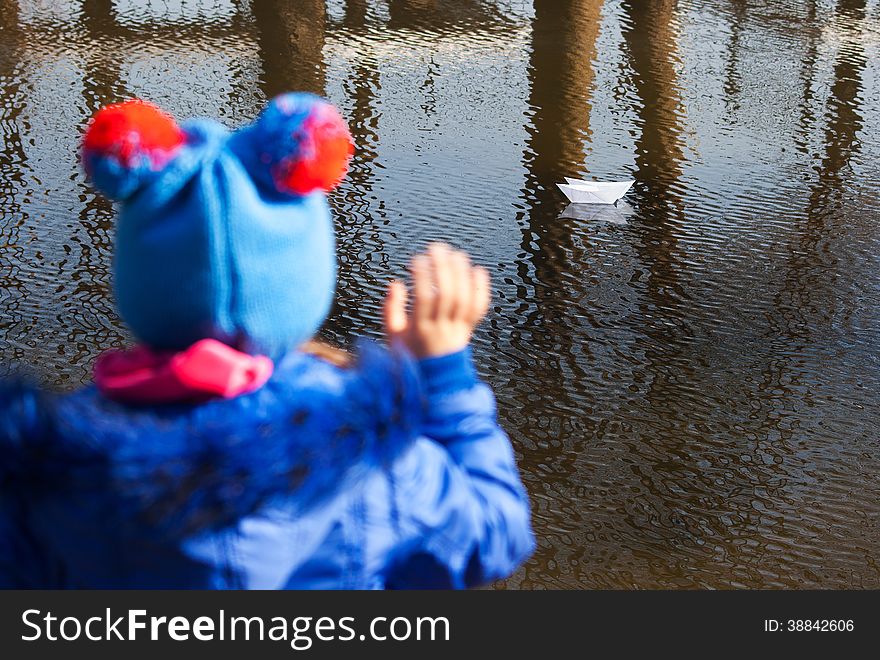 Girl waving a paper boat floating in the creek on spring day