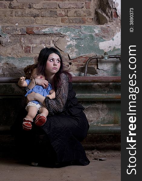 The girl in dark clothes with a doll scaredly looks. The girl in dark clothes with a doll scaredly looks