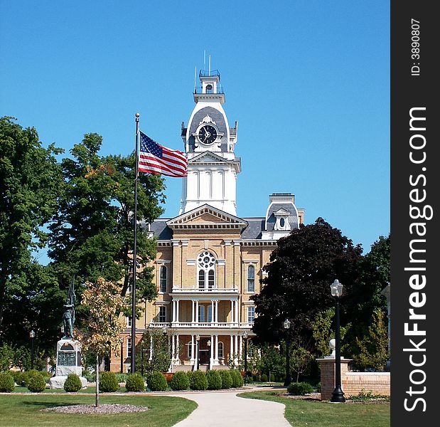 A building with a clock tower with the U.S. flag in front blowing in a brisk breeze.