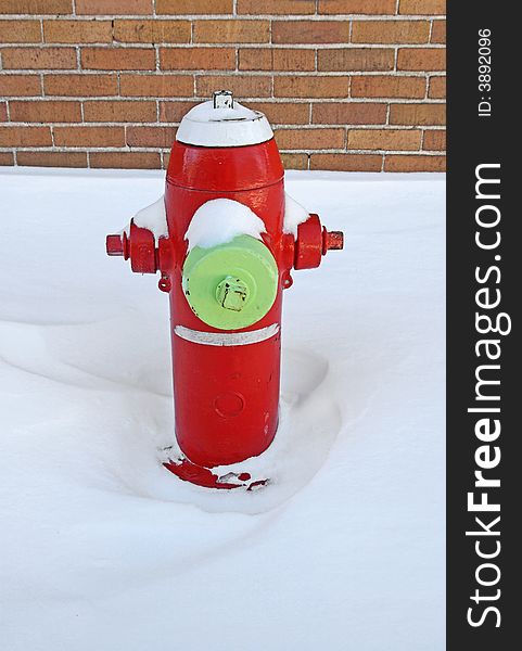 Red fire hydrant covered by snow, near a brick building.