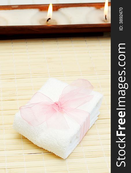 Relaxing spa scene with small white towel with pink organza ribbon around it and candles in the background. Relaxing spa scene with small white towel with pink organza ribbon around it and candles in the background