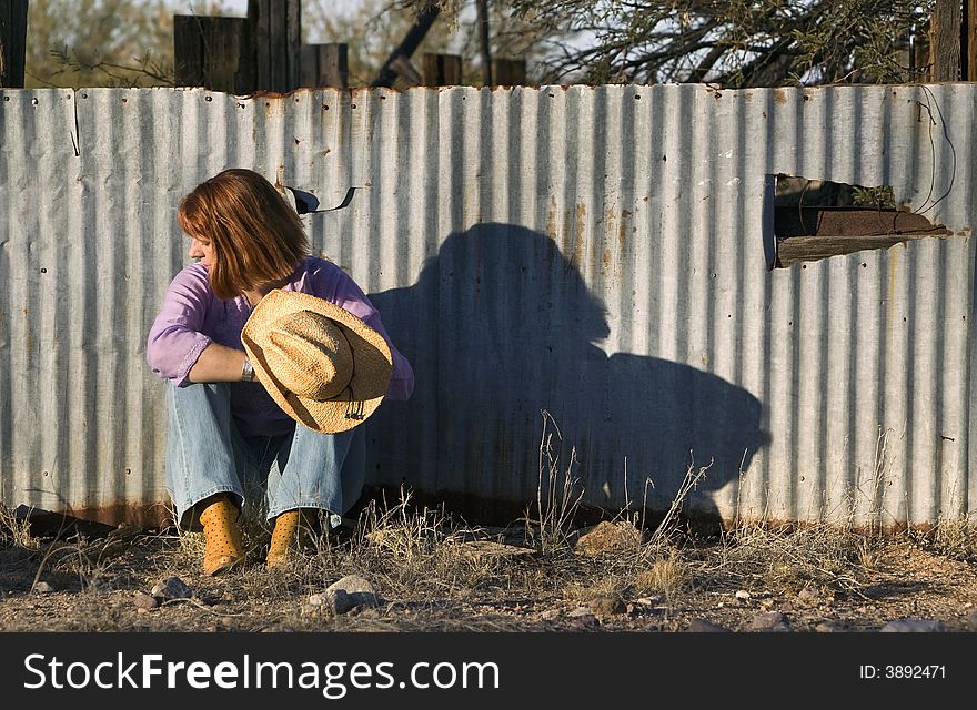 Woman in a Cowboy hat sitting against a Corrugated Metal fence and Looking to her Right. Woman in a Cowboy hat sitting against a Corrugated Metal fence and Looking to her Right.