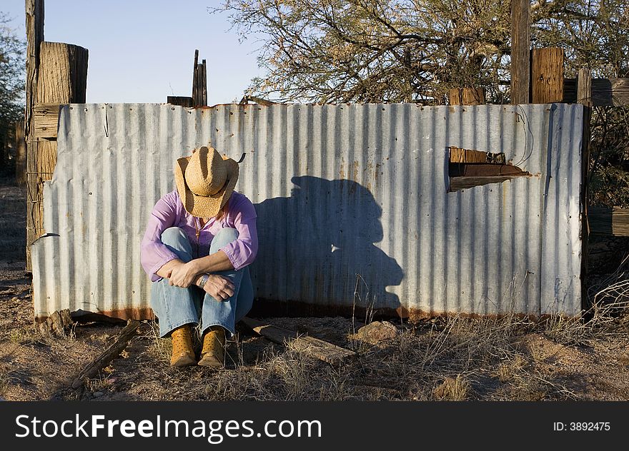 Woman wearing a straw cowboy hat with her head down leaning against a corrugated metal fence. Woman wearing a straw cowboy hat with her head down leaning against a corrugated metal fence.