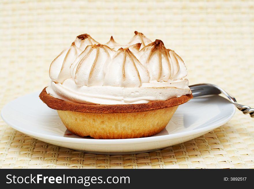 Close-up of miniature lemon meringue cake with silver fork shot on a light wooden background