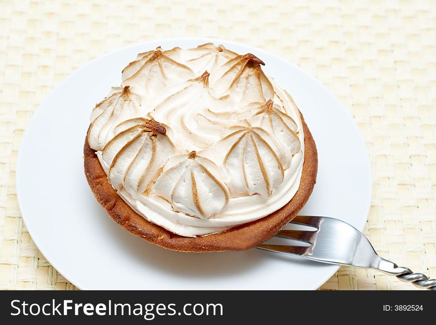 Miniature lemon meringue cake with small silver fork shot on a light wooden background