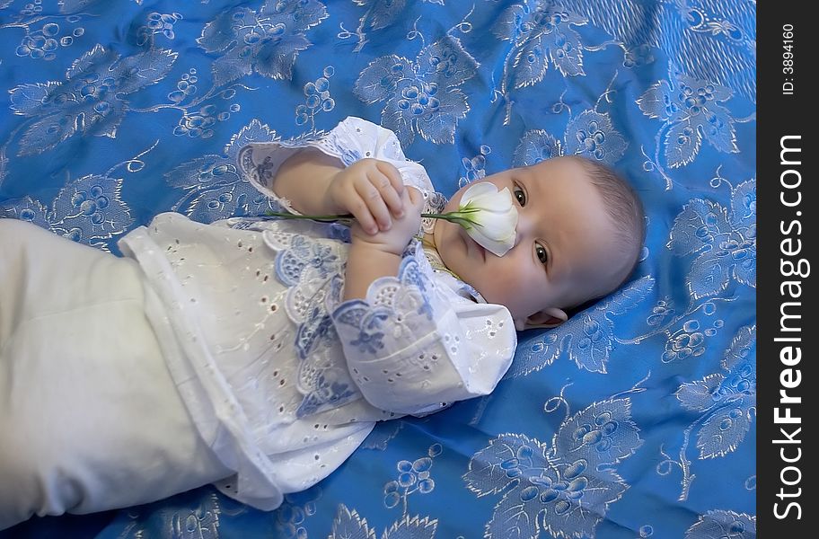 The baby in a shirt with a flower in hands laying on a coverlet. The baby in a shirt with a flower in hands laying on a coverlet