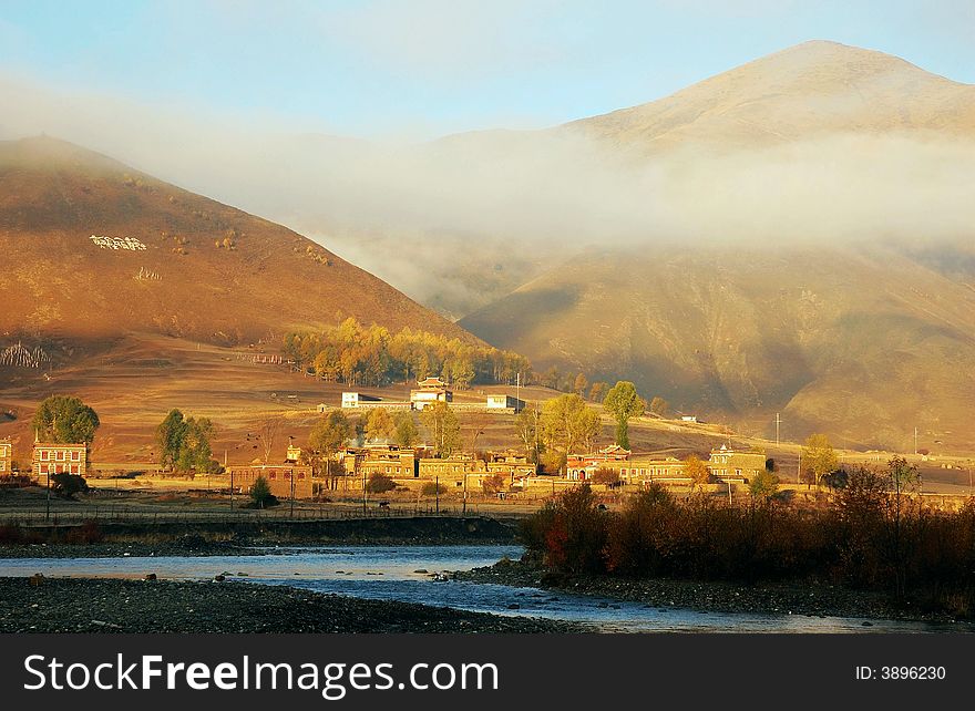 A foggy valley with a river. Some China west style architecture and trees look so beautiful in the sunlight of morning.