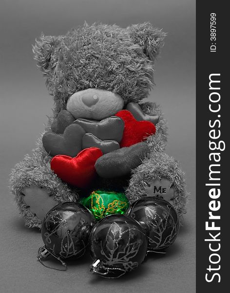 A teddy bear holding hearts in his hands with christmas balls in front. A teddy bear holding hearts in his hands with christmas balls in front.