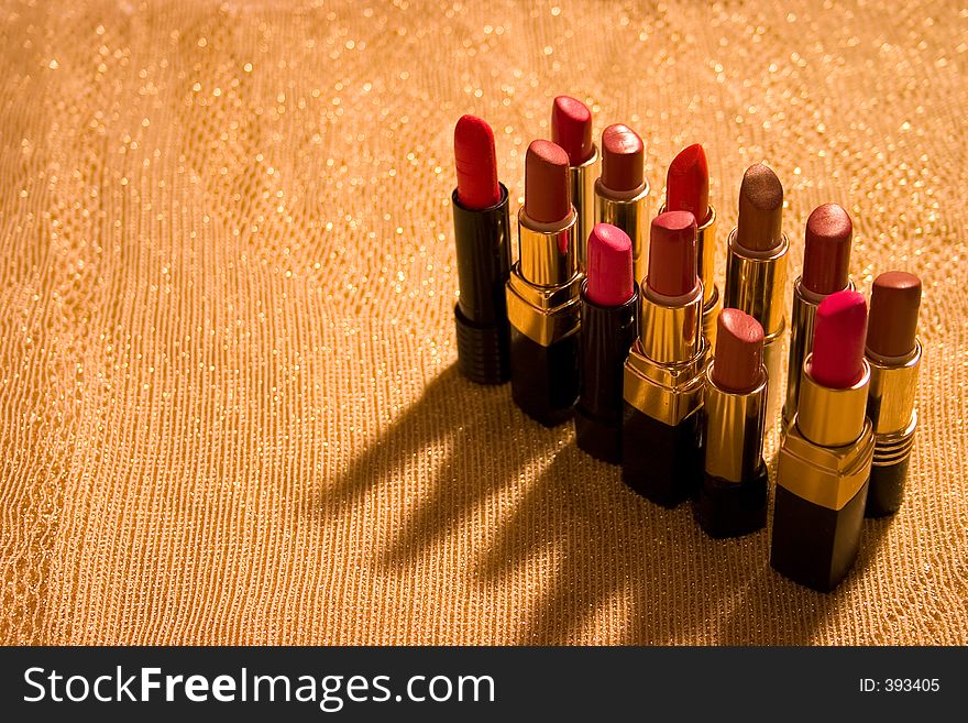 Background of gold shiny material with a dozen open tubes of lipstick. Background of gold shiny material with a dozen open tubes of lipstick.