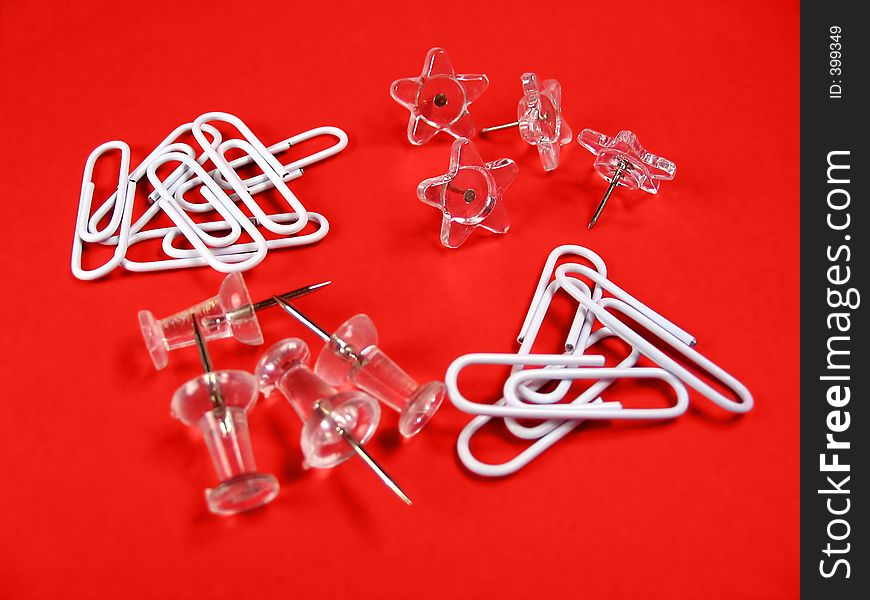 White and transparent paper clips, push pins and star shaped pins on red background. White and transparent paper clips, push pins and star shaped pins on red background