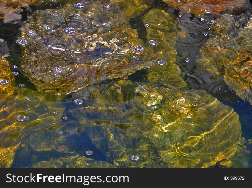 Rocks visible below the pure bubbling water of a creek. Rocks visible below the pure bubbling water of a creek.