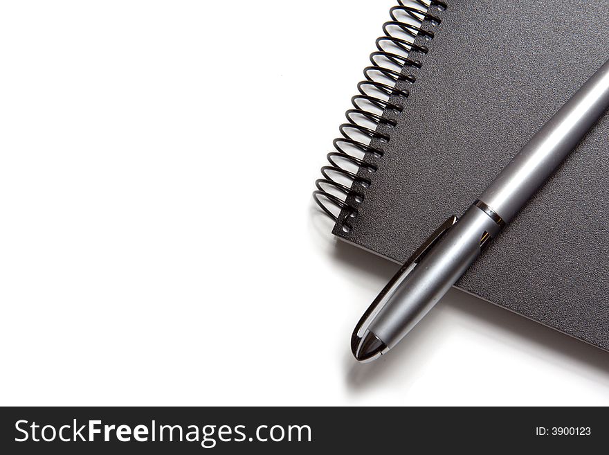 A black notebook and a silver pen on white background. A black notebook and a silver pen on white background