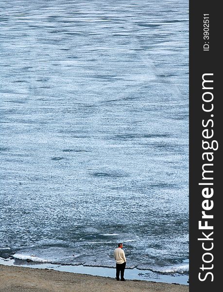 Lone man looking at the frozen water, standing on the shore. Lone man looking at the frozen water, standing on the shore
