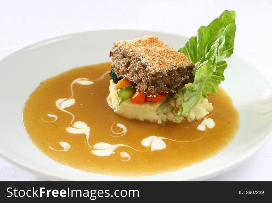 Gourmet meatloaf on a bed of vegetables and mash garnished with trimmed lettuce