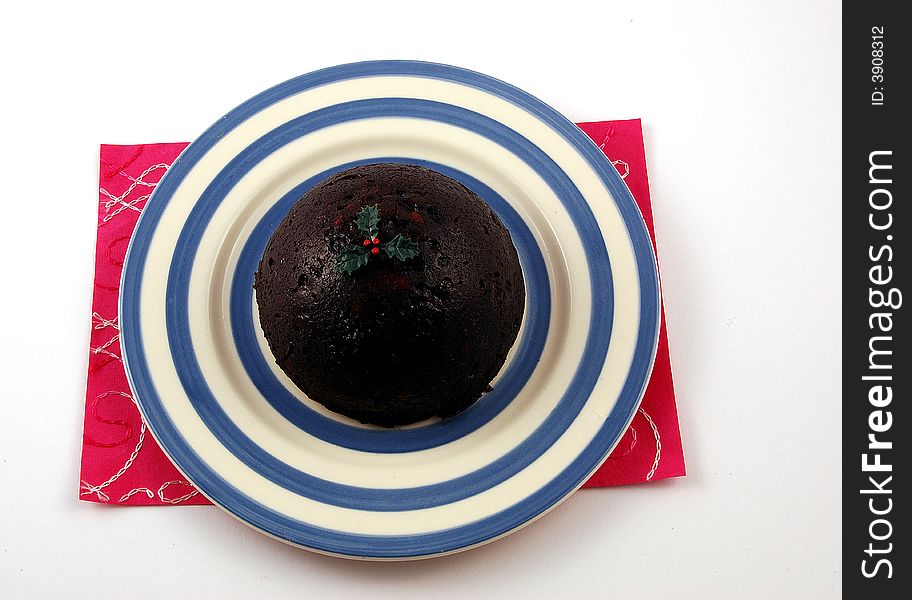 Chirstmas Pudding on a pink mat with a white background. Christmas pudding is a type of pudding traditionally served as part of the Christmas dinner in the UK, Ireland and in other countries where it has been brought by British and Irish immigrants. It has its origins in medieval England, and is sometimes known as plum pudding or just &#x22;pud&#x22;, though this can also refer to other kinds of boiled pudding involving dried fruit. Despite the name &#x22;plum pudding&#x22;, the pudding contains no actual plums due to the pre-Victorian use of the word &#x22;plums&#x22; as a term for raisins. The pudding is traditionally composed of thirteen ingredients, symbolizing Jesus and the Twelve Apostles, including many dried fruits held together by egg and suet, sometimes moistened by treacle or molasses and flavoured with cinnamon, nutmeg, cloves, ginger, and other spices. The pudding is usually aged for a month or more, or even a year; the high alcohol content of the pudding prevents it from spoiling during this time. Chirstmas Pudding on a pink mat with a white background. Christmas pudding is a type of pudding traditionally served as part of the Christmas dinner in the UK, Ireland and in other countries where it has been brought by British and Irish immigrants. It has its origins in medieval England, and is sometimes known as plum pudding or just &#x22;pud&#x22;, though this can also refer to other kinds of boiled pudding involving dried fruit. Despite the name &#x22;plum pudding&#x22;, the pudding contains no actual plums due to the pre-Victorian use of the word &#x22;plums&#x22; as a term for raisins. The pudding is traditionally composed of thirteen ingredients, symbolizing Jesus and the Twelve Apostles, including many dried fruits held together by egg and suet, sometimes moistened by treacle or molasses and flavoured with cinnamon, nutmeg, cloves, ginger, and other spices. The pudding is usually aged for a month or more, or even a year; the high alcohol content of the pudding prevents it from spoiling during this time.