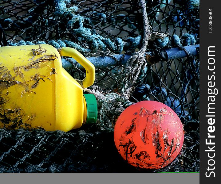 A fishing net on whitch there is a red buoy, an old empty yellow drum and blue moorings