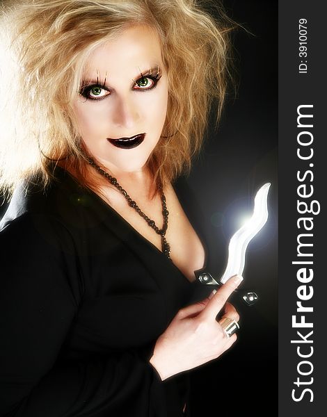 Beautiful 40 year old woman dressed as witch holding dagger over black background.