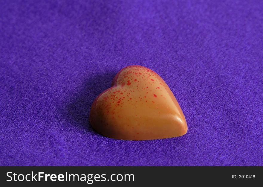 Heart shape chocolate with red dots over a silky violet background.