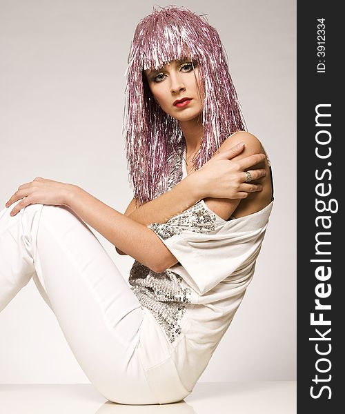 Beautiful girl dressed for carnival wearing glossy pink wig and silver blouse on light background. Beautiful girl dressed for carnival wearing glossy pink wig and silver blouse on light background