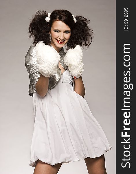 Beautiful brunette winter girl wearing furry gloves and white dress on light background