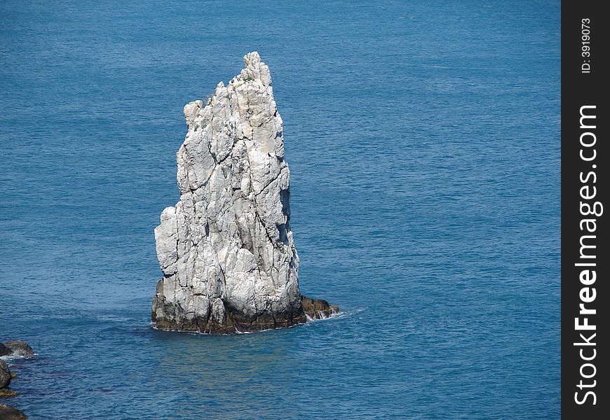 Lonely rock near a coast looks like a sailing-vessel