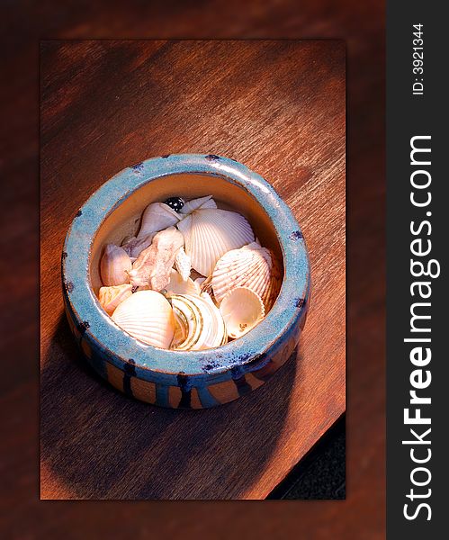 A ceramic bowl of seashells on a wooden table