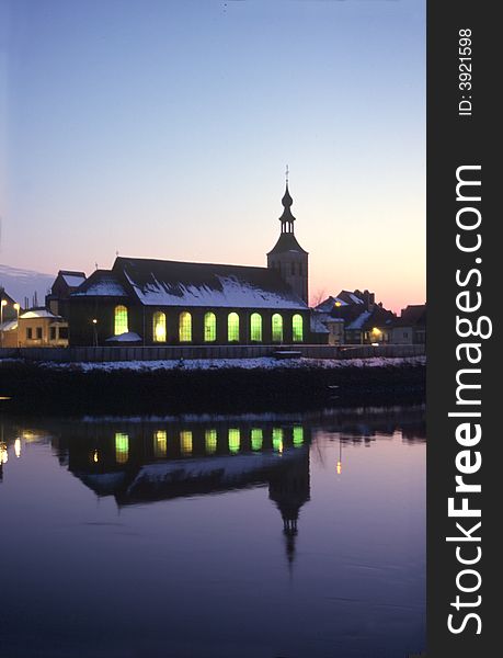 Small church at christmas time close to border river, reflection of the lights in the water at night time. Small church at christmas time close to border river, reflection of the lights in the water at night time