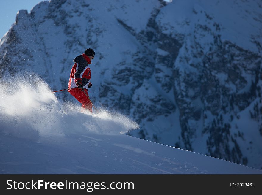 Powder skiing in front of huge mountain - selective focus lit from behind. Powder skiing in front of huge mountain - selective focus lit from behind