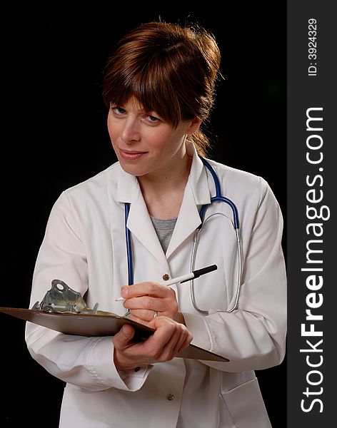 Attractive young lady doctor in white coat with stethosope making notes - on black background. Attractive young lady doctor in white coat with stethosope making notes - on black background