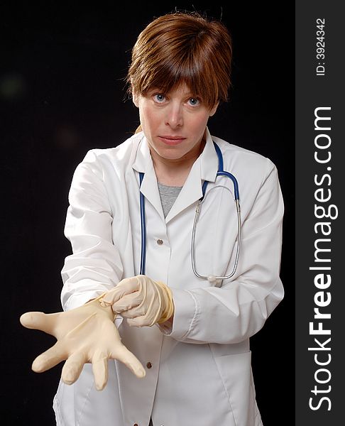 Cute young lady doctor or nurse putting on latex gloves, on black