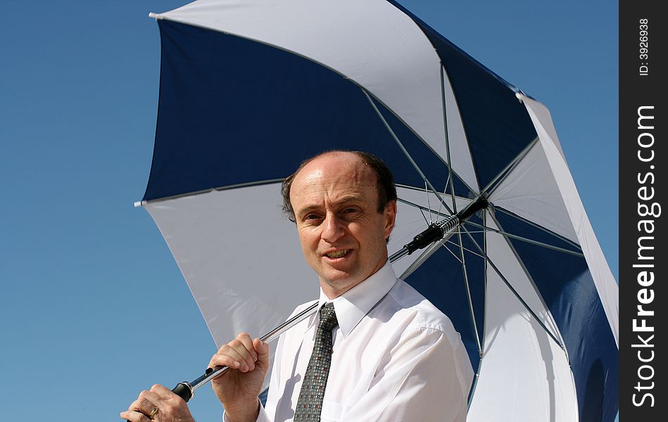 Businessman on the beach in business attire with a white and blue umbrella and a beautiful blue sky behind him, asking the question, do you have enough cover. Businessman on the beach in business attire with a white and blue umbrella and a beautiful blue sky behind him, asking the question, do you have enough cover