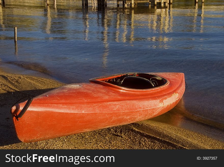 A red kayak half on the beach and half in the water ready to go.